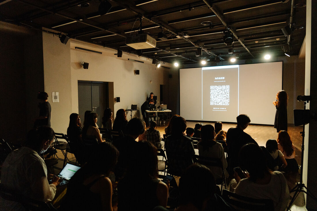 場館全景：觀眾坐滿，遠方投影幕顯示投票 QR code
